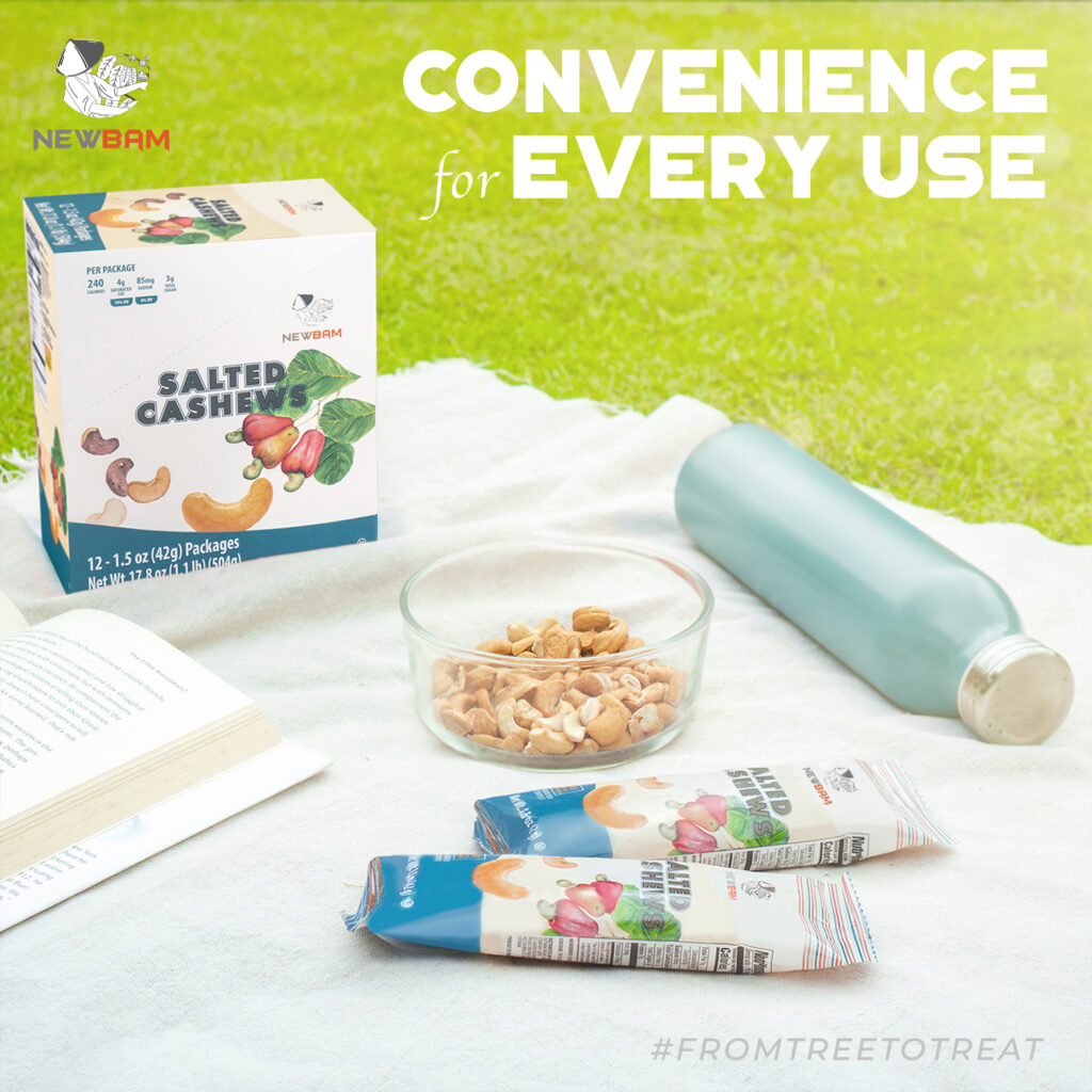 NEWBAM Sea Salt cashew box and individual packs on a picnic blanket beside a book and a bowl of cashews.