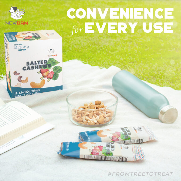 NEWBAM Sea Salt cashew box and individual packs on a picnic blanket beside a book and a bowl of cashews.