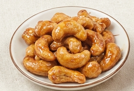 Close-up of Honey cashews with their glossy coating on a light porcelain dish.